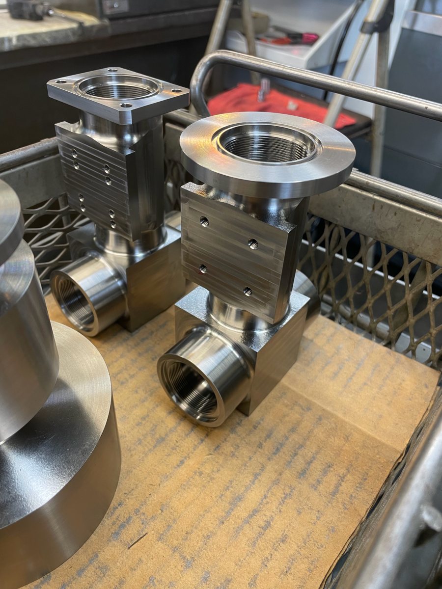 Two stainless valve bodies with threaded ports and flanges