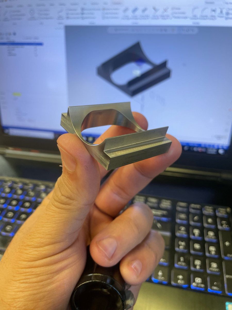Small machined part held in hand with its CAD model behind