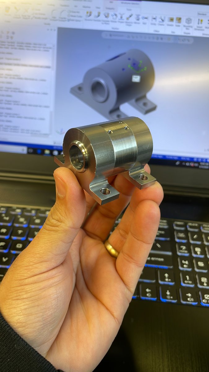 Machined stainless bracket held in hand with its CAD model behind